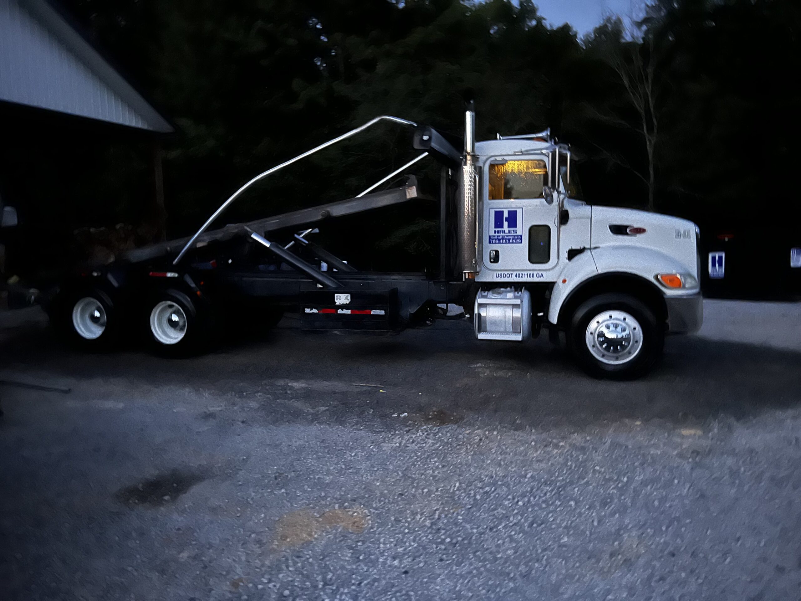 Roll-off truck lifting a dumpster container during pickup service.